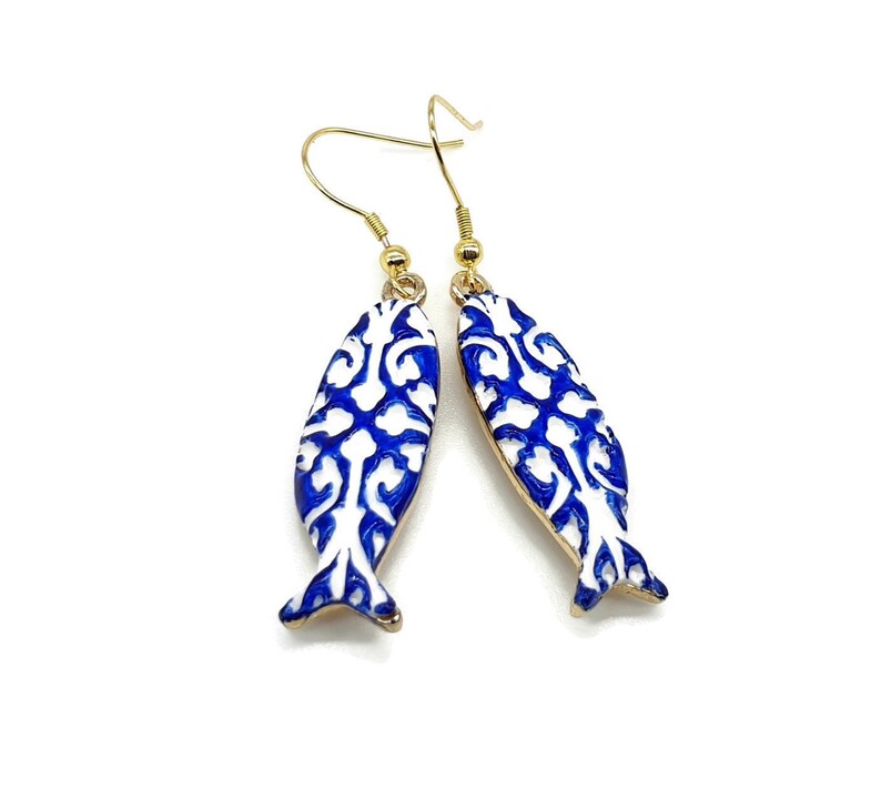 May include: A pair of blue and white fish-shaped earrings with a gold hook. The fish have a white background with a blue floral pattern.