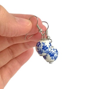Op de afbeelding: Een paar blauwe en witte porseleinen oorbellen met een bloemenmotief. De oorbellen zijn rond en hebben zilveren haakjes.