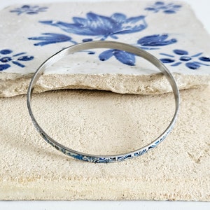 May include: A silver bangle bracelet with a blue and white floral pattern.