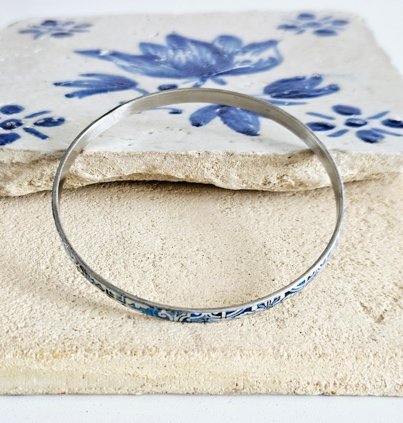 May include: A silver bangle bracelet with a blue and white floral pattern.