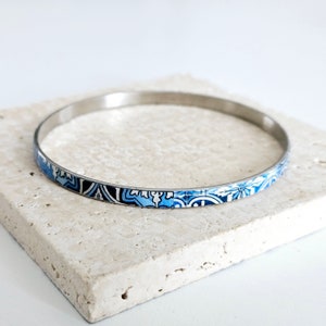 May include: A silver bangle bracelet with a blue and white patterned design.