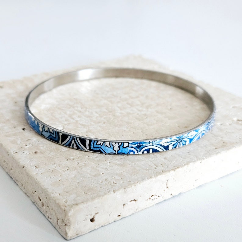 May include: A silver bangle bracelet with a blue and white patterned design.
