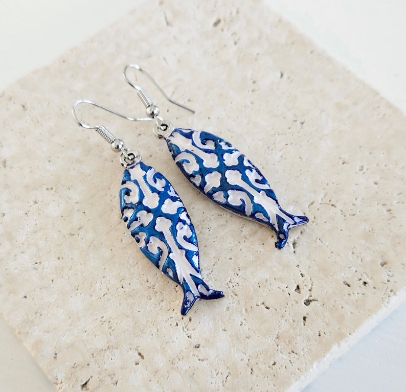 May include: A pair of silver fish-shaped earrings with a blue and white patterned design.