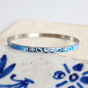 May include: A silver bangle bracelet with a blue and white patterned design. The pattern is reminiscent of traditional Portuguese tiles.