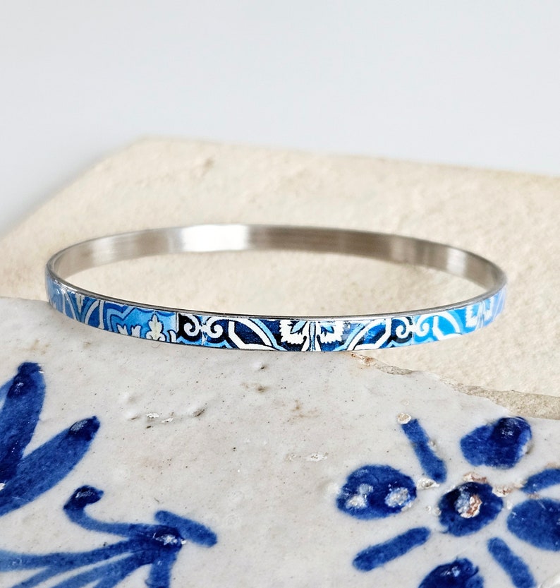 May include: A silver bangle bracelet with a blue and white patterned design. The pattern is reminiscent of traditional Portuguese tiles.
