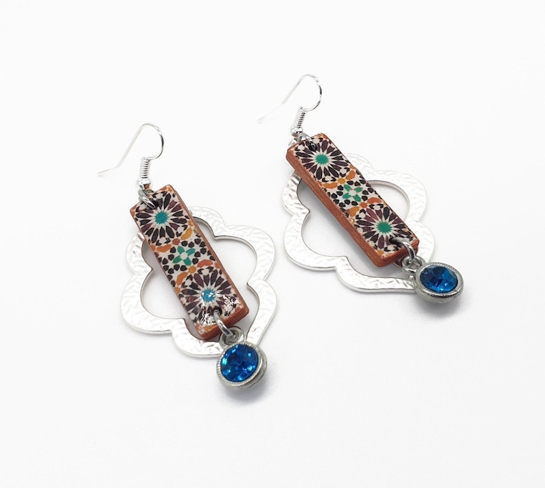 Peut inclure: Une paire de boucles d'oreilles en argent avec un motif g&eacute;om&eacute;trique. Chaque boucle d'oreille pr&eacute;sente un pendentif rectangulaire avec un motif de carrelage marocain color&eacute; et un pendentif en cristal bleu.