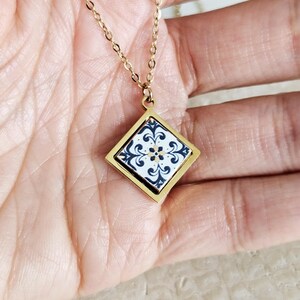May include: Gold chain necklace with a square pendant featuring a blue and white tile design.