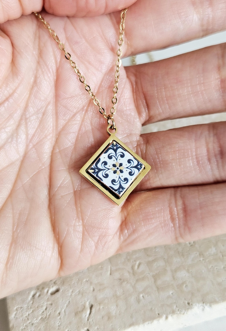May include: Gold chain necklace with a square pendant featuring a blue and white tile design.