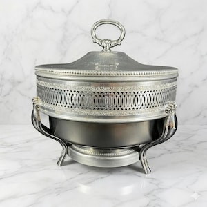 May include: Silver-plated serving dish with a lid and handle. The dish has a decorative pierced design around the middle and is supported by three curved legs. The lid features a loop handle.