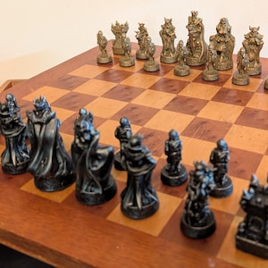 May include: A chess set with detailed black and bronze chess pieces on a wooden board with a chequered pattern. The pieces are arranged ready for a game. The board is made of wood.