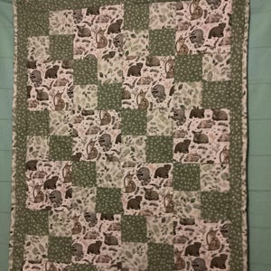 Pode incluir: Um edredão feito à mão com um design de patchwork. Os quadrados alternam entre um padrão de animais da floresta, incluindo raposas e ursos, e quadrados verdes lisos com bolinhas brancas. O edredão é bordado com um tecido verde pontilhado.