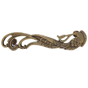 May include: An antique bronze-colored drawer pull with a decorative peacock design. The pull features intricate details, including a stylized peacock and flowing, ornate patterns. The hardware is approximately 6 inches long.
