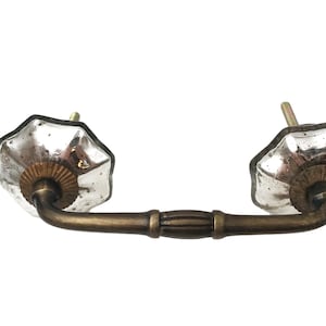 May include: Antique-style drawer pull with two faceted, mercury glass knobs and a bronze-toned metal handle. The knobs have a starburst design and are attached to the handle with a curved stem. The hardware is designed for furniture.