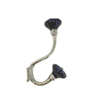 May include: A decorative wall hook with a curved, silver-toned metal arm. The hook features two dark blue, rounded ceramic knobs. The hook is designed for hanging items and adds a touch of elegance to any space.