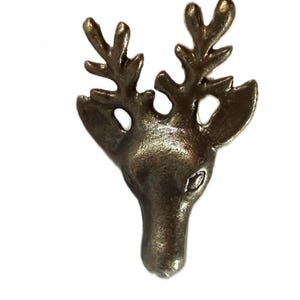 May include: A bronze-colored metal reindeer head with detailed antlers and a textured surface. The reindeer head is a decorative element, possibly for jewelry or crafts, and is set against a white background.