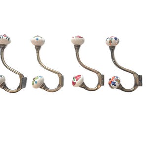 May include: Four decorative wall hooks with a vintage aesthetic. Each hook features a curved, metallic arm and a ceramic knob with a floral pattern in various colors. The hooks are designed for hanging items and add a touch of elegance to any space.