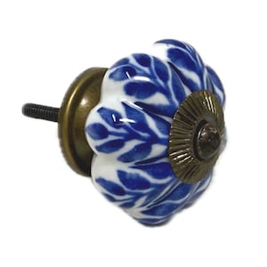 May include: A decorative cabinet knob with a white and blue floral design. The knob has a round, fluted shape and a brass-colored base and screw. The blue pattern resembles leaves.