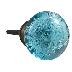 May include: A round, light blue glass cabinet knob with a bubble design. The knob has a bronze-colored metal base and screw. This decorative hardware is suitable for drawers, cabinets, and furniture.