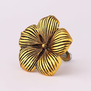 May include: A decorative, golden flower-shaped cabinet knob. The knob features a detailed design with textured petals and a dark, contrasting finish. The hardware is designed for easy installation on drawers or cabinets.