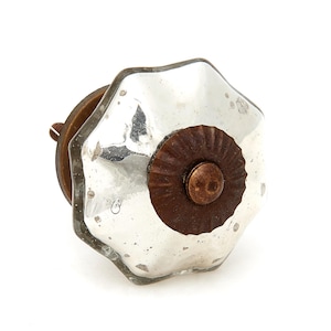 May include: A decorative cabinet knob with a clear, faceted glass face and a distressed, antique silver finish. The knob features a dark brown, circular base and a copper-colored center, adding a vintage touch to furniture or decor.
