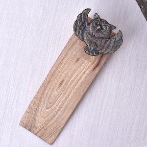 May include: A wooden serving board with a bronze-colored owl figurine attached. The owl has outstretched wings and detailed feathering. The board is rectangular with a natural wood grain finish, suitable for serving appetizers or small dishes.