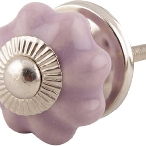 May include: A decorative cabinet knob with a light purple, flower-shaped ceramic handle. The knob features a silver metal base and a threaded post for easy installation. The knob measures approximately 1.5 inches in diameter.