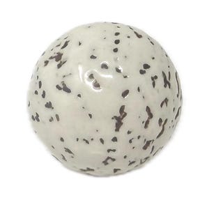 May include: A spherical ceramic object with a glossy off-white glaze featuring a speckled pattern of dark brown and black spots distributed across the surface. The round item has a smooth, reflective finish and a uniform, circular shape.