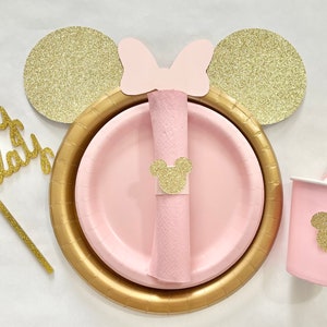 May include: Pink and gold Mickey Mouse themed party supplies. The set includes a cake topper that says "happy birthday", a napkin ring, a paper cup, and a straw with a Mickey Mouse head on it.