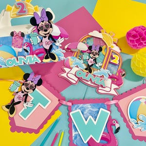 May include: A set of party decorations featuring Minnie Mouse in a swimsuit and heart-shaped sunglasses, including a box, a cake topper, and a banner spelling TWO. The items are decorated with flamingos, beach balls, and the name OLIVIA.