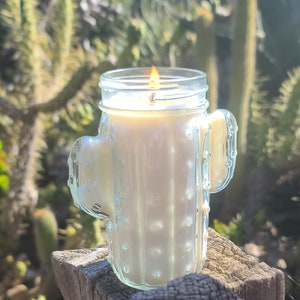 May include: A clear glass candle holder shaped like a cactus with a white candle inside. The candle is lit and the flame is visible.