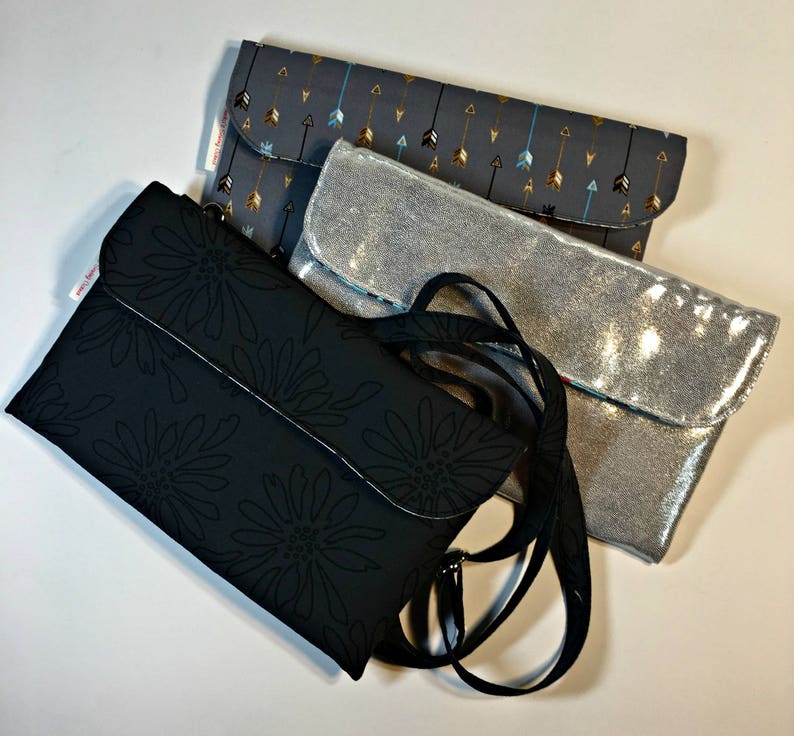 May include: Three different fabric clutches, one black with a floral pattern, one silver with a sparkly finish, and one gray with a pattern of arrows. The black clutch has a black strap.