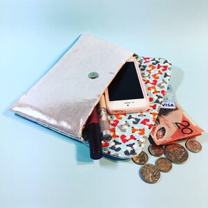 May include: A silver clutch purse with a fox print lining. The purse is open and contains a smartphone, lipstick, a credit card, and Australian currency.