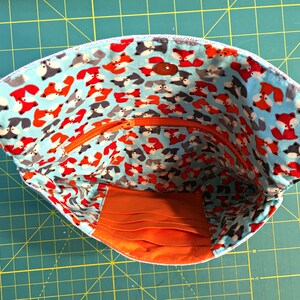 May include: A blue fabric pouch with a zipper closure and a bright orange lining. The pouch is decorated with a repeating pattern of red and gray foxes on a light blue background.