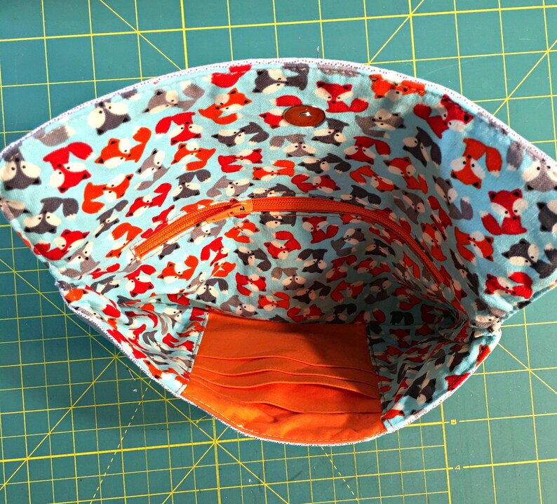 May include: A blue fabric pouch with a zipper closure and a bright orange lining. The pouch is decorated with a repeating pattern of red and gray foxes on a light blue background.