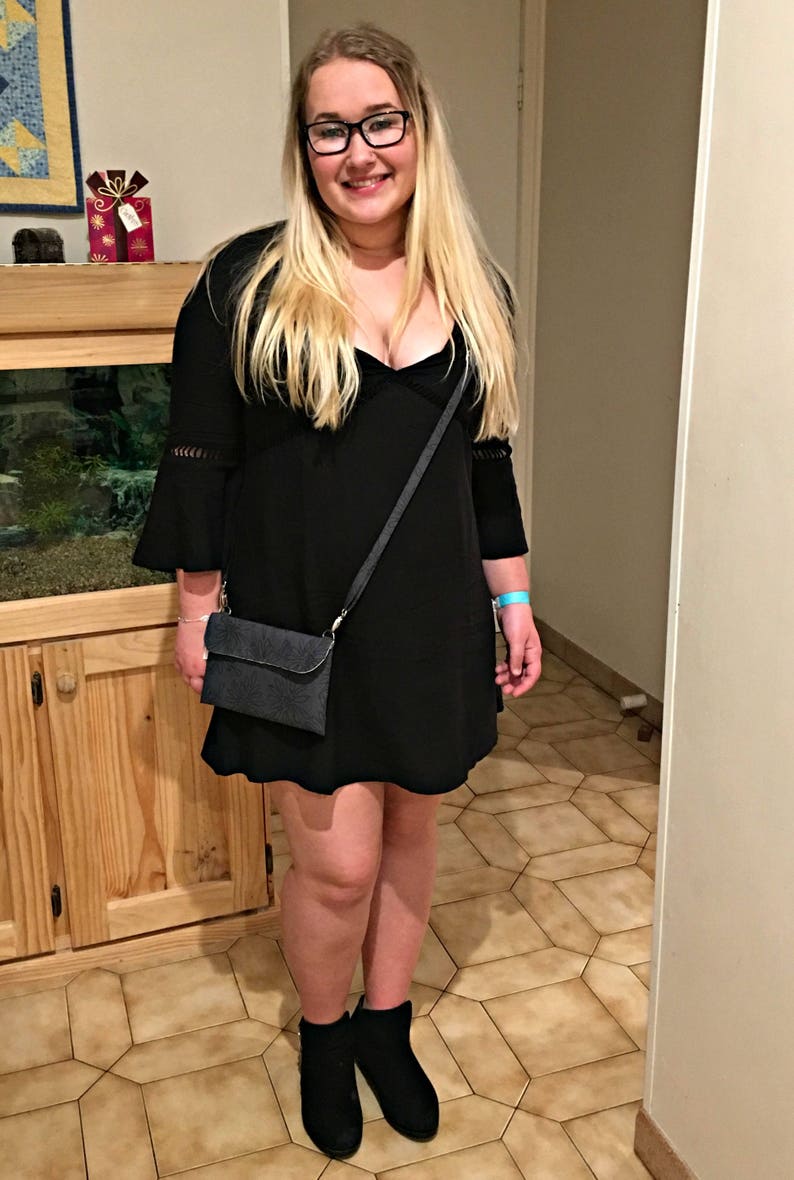 May include: A woman wearing a black dress with a plunging neckline and a black crossbody bag. She is wearing black ankle boots and has long blonde hair.