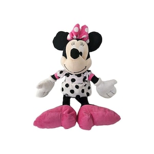 Peut inclure: Une peluche Minnie Mouse, avec une t&ecirc;te et des oreilles noires, un n&oelig;ud rose &agrave; pois blancs et une robe assortie. La poup&eacute;e a des gants blancs, des jambes noires et de grands pieds roses. La poup&eacute;e est debout.