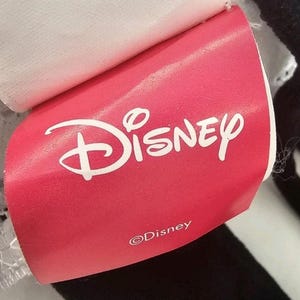 Peut inclure: Une &eacute;tiquette rouge Disney avec le logo Disney en blanc. L'&eacute;tiquette est attach&eacute;e &agrave; un article noir et blanc. Le logo Disney est une &eacute;criture stylis&eacute;e avec une ic&ocirc;ne de ch&acirc;teau au-dessus du mot Disney. L'&eacute;tiquette comprend &eacute;galement le symbole du droit d'auteur et le mot "Disney".