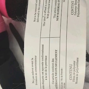 Pode incluir: Uma etiqueta retangular branca de cuidados do produto com texto preto em ingl&ecirc;s e franc&ecirc;s. O texto especifica que o artigo cont&eacute;m apenas material novo, especificamente fibras de poli&eacute;ster e espuma de poliuretano, n&uacute;mero QC-001864.