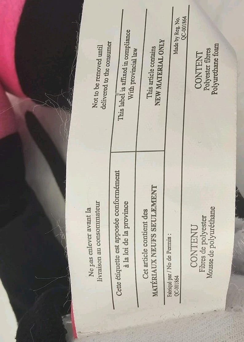 Pode incluir: Uma etiqueta retangular branca de cuidados do produto com texto preto em ingl&ecirc;s e franc&ecirc;s. O texto especifica que o artigo cont&eacute;m apenas material novo, especificamente fibras de poli&eacute;ster e espuma de poliuretano, n&uacute;mero QC-001864.