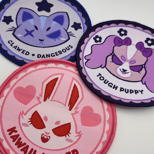 May include: Three embroidered patches with cartoon animal characters. The first patch is purple and blue with a cat and the text "Clawed & Dangerous". The second patch is purple and pink with a dog and the text "Tough Puppy". The third patch is pink with a bunny and the text "Kawaii Killer".