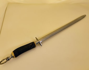 May include: A steel knife sharpener with a dark brown antler handle and a silver metal guard. The sharpener has a long, slender, gray steel rod and a ring at the end of the handle.