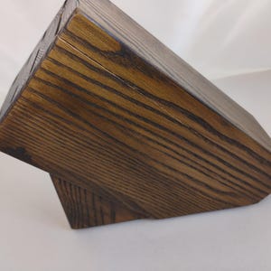 May include: A dark brown wooden knife block with a visible wood grain pattern. The block features a slanted top surface with multiple slots for storing kitchen knives, constructed from solid wood with a stained finish and a sturdy base.