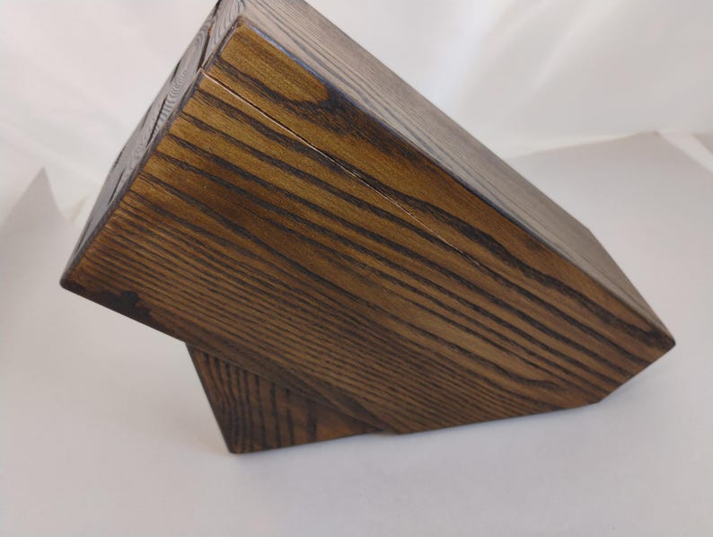May include: A dark brown wooden knife block with a visible wood grain pattern. The block features a slanted top surface with multiple slots for storing kitchen knives, constructed from solid wood with a stained finish and a sturdy base.