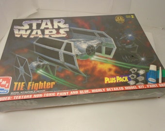 May include: A Star Wars TIE Fighter model kit with a plus pack of paint and glue. The box features a TIE Fighter in flight with a red and orange background. The box also includes the text "STAR WARS" and "TIE Fighter".