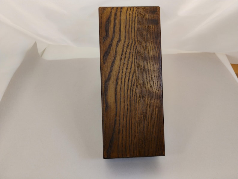 May include: A rectangular wooden block with a dark brown finish and a prominent, vertical wood grain pattern. The object has clean, straight edges and a smooth, flat surface, showcasing the natural texture and deep brown tones of the wood.
