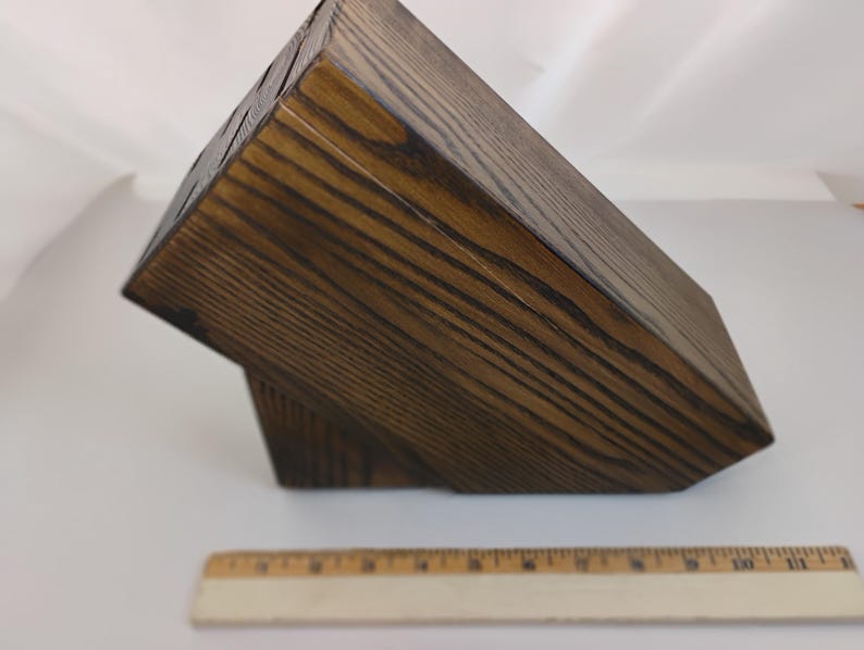 May include: A dark brown, stained wooden knife block with a visible wood grain pattern, featuring multiple slots on the top surface for knife storage. A wooden ruler is positioned in front, showing the block is approximately 11 inches long.