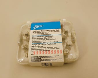 May include: A 29-piece Ateco decorating tube set in a clear plastic storage case. The set includes 26 decorating tubes, a coupler, and 2 flower nails. A blue and white paper label wraps around the center, displaying the product name and details.