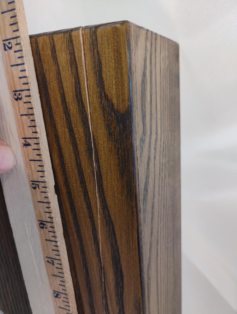 May include: A rectangular wooden block with a dark brown stained finish and visible wood grain, positioned next to a wooden ruler that shows a measurement of approximately 6.5 inches along the side of the object.