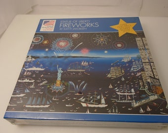 May include: A 1000 piece jigsaw puzzle box featuring a colorful illustration of fireworks over the Statue of Liberty and New York City. The box is blue with a red, white, and blue American flag in the top left corner. The title of the puzzle is "Statue of Liberty Fireworks" by Kathy Jacobsen.