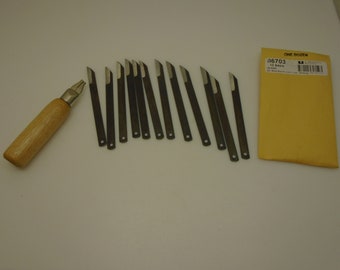 Könnte beinhalten: Ein Satz Holzschnitzwerkzeuge, darunter ein Messer mit Holzgriff und ein Dutzend Ersatzklingen. Die Klingen sind aus dunklem Metall mit scharfer Kante. Ein gelber Umschlag mit Text ist ebenfalls enthalten.